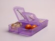 Vitamins in an open purple box with a timetable for taking on a pale pink background.