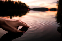 Closeup Of A Hand Touching The Water Making Smooth Waves On The Surface In A Lake In Sunset