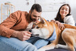 © LIGHTFIELD STUDIOS - akita inu dog smelling hand of happy man near blurred woman.