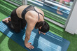 An athletic woman does a cat pose stretch on a yoga mat at the gym. Back arched. Warming up before a full body workout.