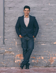 Wall Mural - Success looks this good. Portrait of a handsome young businessman standing against a face brick wall with his hands in pockets.