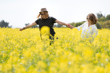 Two young women are walking and having fun in nature. Large field of yellow flowers. Sunny day.