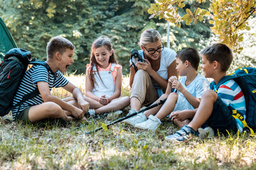 Wall Mural - Group of children sitting on grass in the forest with their teacher.They learn about nature and wildlife.	