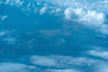 Wall Mural - view of the earth below while flying above the clouds, mountainous terrain through atmospheric haze, view from above