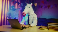A Woman In A Pigeon Mask Is Dancing In The Background, And A Young Man In A Unicorn Mask Is Sitting At A Table. Multicolored Lighting. Masquerade