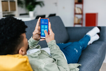 Young latin american man hands using IOT smart home app on smartphone at home - Automation control service