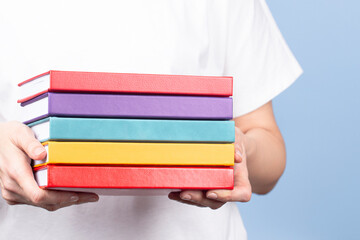 Wall Mural - Female hands holding pile of books over light blue background. Education, self-learning, book swap, hobby, relax time