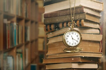 Wall Mural - old clock on a chain with stack books on library background. retro clock as a symbol of time a books