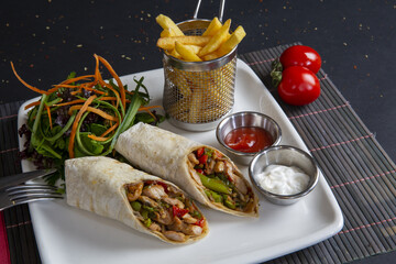 Wall Mural - Top view shot of chicken wraps, salad, fries, sources, and tomatoes on a white plate