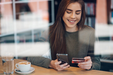 Woman using smartphone and a credit card for online shopping in a cafe