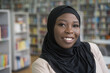 Beautiful confident muslim woman wearing black hijab looking at camera, copy space. Portrait of smiling African student standing in university library, education concept