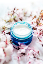 Herbal Spa Cosmetic Cream With Pink Cherry Flowers In A Blue Glass Jar. Hygienic Skincare Lotion Product.