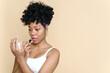 © etonastenka - Beautiful afro american woman applying lipstick on her lips and looking in the mirror on a beige background. opy space