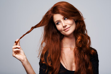 Poster - Time for a change. Studio shot of a young woman holding her beautiful red hair against a gray background.