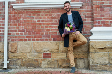 Sticker - Its for the love of my life. Portrait of a handsome young man standing against a brick wall with a bunch of flowers in hand.