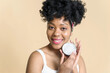 © etonastenka - Organic cosmetic concept. Smiling african american woman holding jar of cream on beige background and looking at camera.