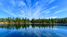 Panoramic Scenic View Of Lake Tabeaud Surrounded By Pine And Cedar Trees Under Beautiful Blue Sky