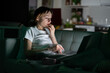 Young anxious woman lying on sofa staring at laptop screen at night, reading about depression symptoms in internet. Addicted girl can not stop scrolling news media before bedtime. Anxiety, depression.