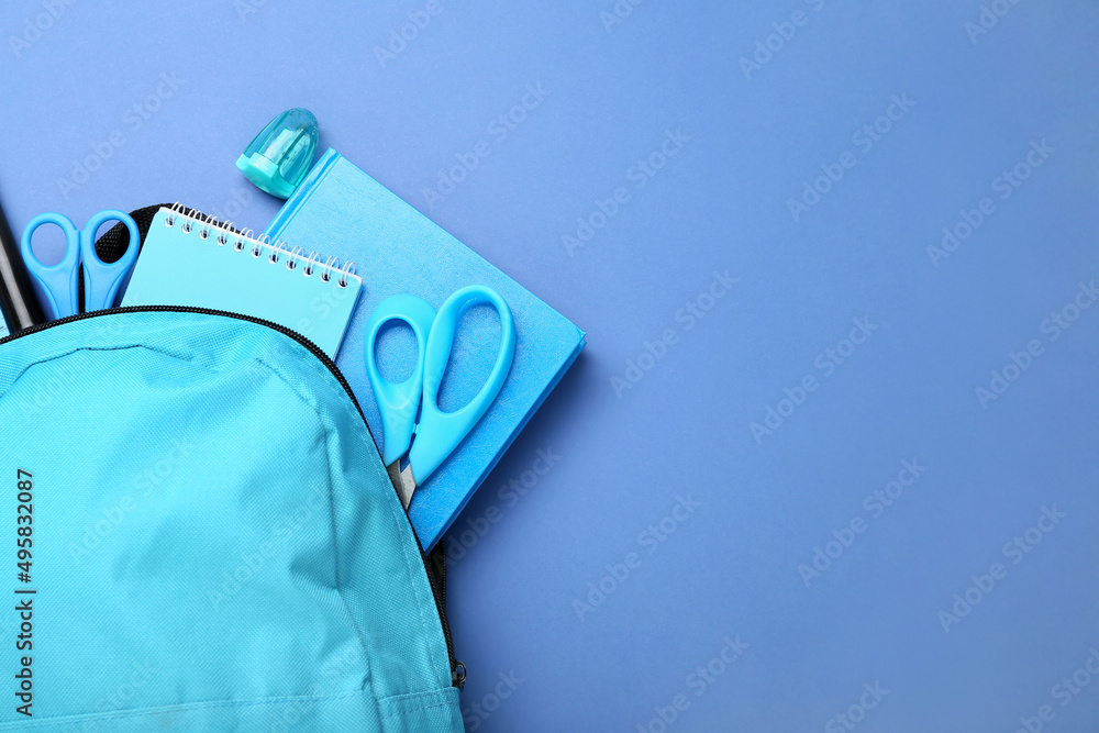 Backpack with stationery on blue background, closeup