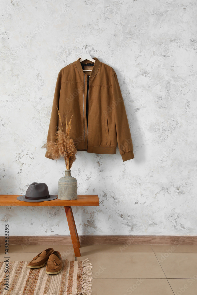 Wooden bench with hat, vase, shoes and jacket hanging on light wall