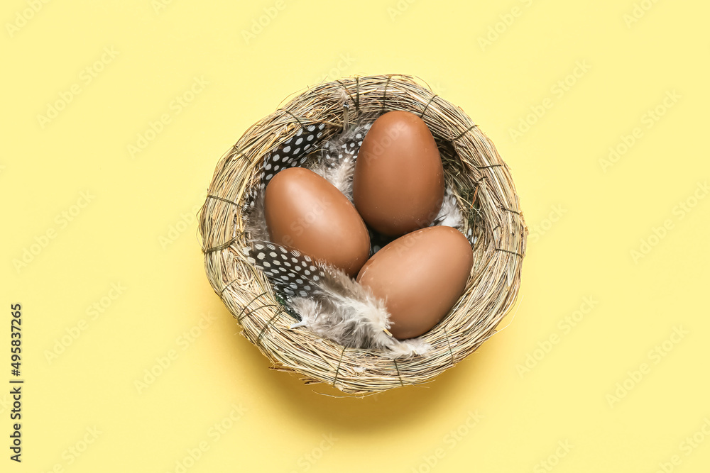 Nest with delicious chocolate eggs on yellow background