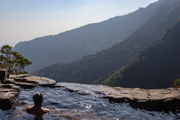 man enjoying the pristine view at natural swimming pool at mountain cliff from top angles