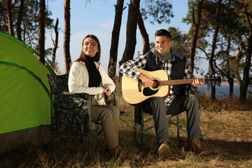 Canvas Print - Couple with guitar resting in camping chairs near tent outdoors