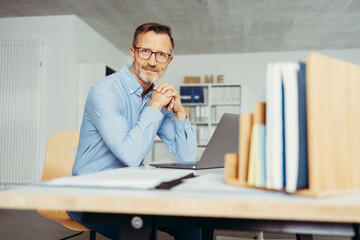 smiling man sitting at his desk in front of a laptop in his office