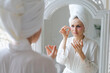 © Екатерина Переславце - Under eyes for eyes for puffy, anti-wrinkle and dark circles. Eye patch concept. Satisfied woman in bathrobe and white towel on head applying pink eye patches while looking at mirror