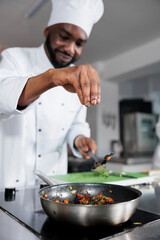 Wall Mural - Head cook throwing fresh chopped herbs in pan to improve taste of meal while in professional kitchen. Master chef seasoning dish prepared for food contest held at fine dining restaurant.