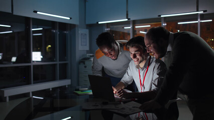 Multiethnic colleagues work on laptop and smile in dark office