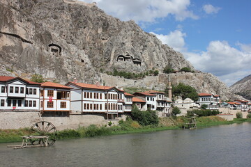 Wall Mural - Ancient stone rock tombs of kings on the hills and traditional old wooden houses. Historical village next to river and a water mill wheel in the water. 