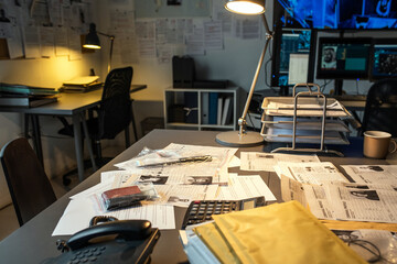Poster - Part of workplace of modern fbi agent with documents, evidences, calculator and telephone on desk lit by lamp in small office