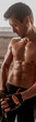 © Yaroslav Astakhov - Vertical photo of muscular male in training gloves holding fitness straps in the sport club