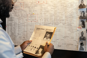 Aufkleber - Young African American male FBI agent looking through criminal profile of gang leader in front of board with map and photos of suspects