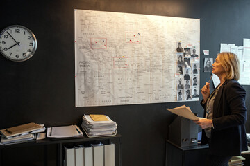 Aufkleber - Mature blond serious female investigator looking at map on board while thinking of ideas about possible location of serial killer