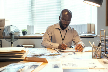 Aufkleber - Young serious male investigator learning personal information of gang leader or serial killer while sitting by desk with criminal profiles