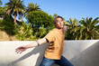 Man dancing with arm extended outdoors with blue sky and palm trees 