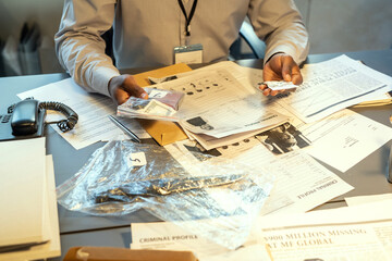 Aufkleber - Hands of young contemporary FBI agent or detective holding evidences in packets while sitting by workplace with criminal profiles
