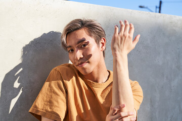 Man dancing showing back of hand by wall outdoors with trees