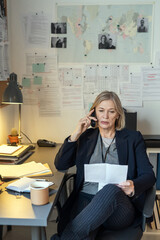 Aufkleber - Blond mature female detective in formalwear sitting in investigation office and questioning witness or victim on the phone