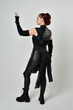 © faestock - Full length portrait of pretty red haired female model wearing black futuristic scifi leather costume. Dynamic standing poses with gestural hands, facing backwards away from  on a white studio backgro