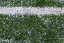 The Football Field With Artificial Green Grass Is Covered With A Light Layer Of Snow. Early Spring. Green Grass On The Football Field Is Visible From Under The Snow. Amateur Football Field