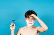 Worried shirtless teenager boy looking at camera while holding razor on his hands. Shaving fear on puberty concept.