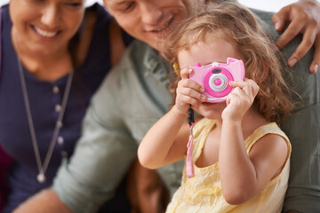 Wall Mural - She started practising her photography for their trip. A little girl playing with a camera as she sits with her parents.