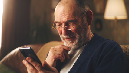 elderly man smiling and watching funny videos on social networks using smartphone and resting in the