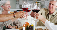Heres To Friends Who Feel Like Family. Shot Of Two Happy Couples Sitting Down For Lunch And Toasting With Wine Glasses At Home.