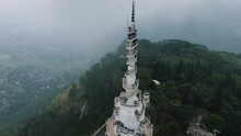 Beautiful High White Ambuluwawa Tower Between The Green Nature Where Several Tourists At The Top Of The Spiraling Stairs Enjoy The View Of Sri-Lanka On A Misty Day. Backwards Drone Tilt Shot