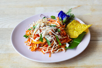 Wall Mural - Stir Fried Rice Noodle Thai style with crab and fried dumplings or Thai people call Pad thai in plate on wooden table.