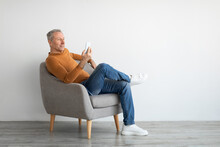 Portrait Of Mature Man Using Smartphone Sitting On Armchair